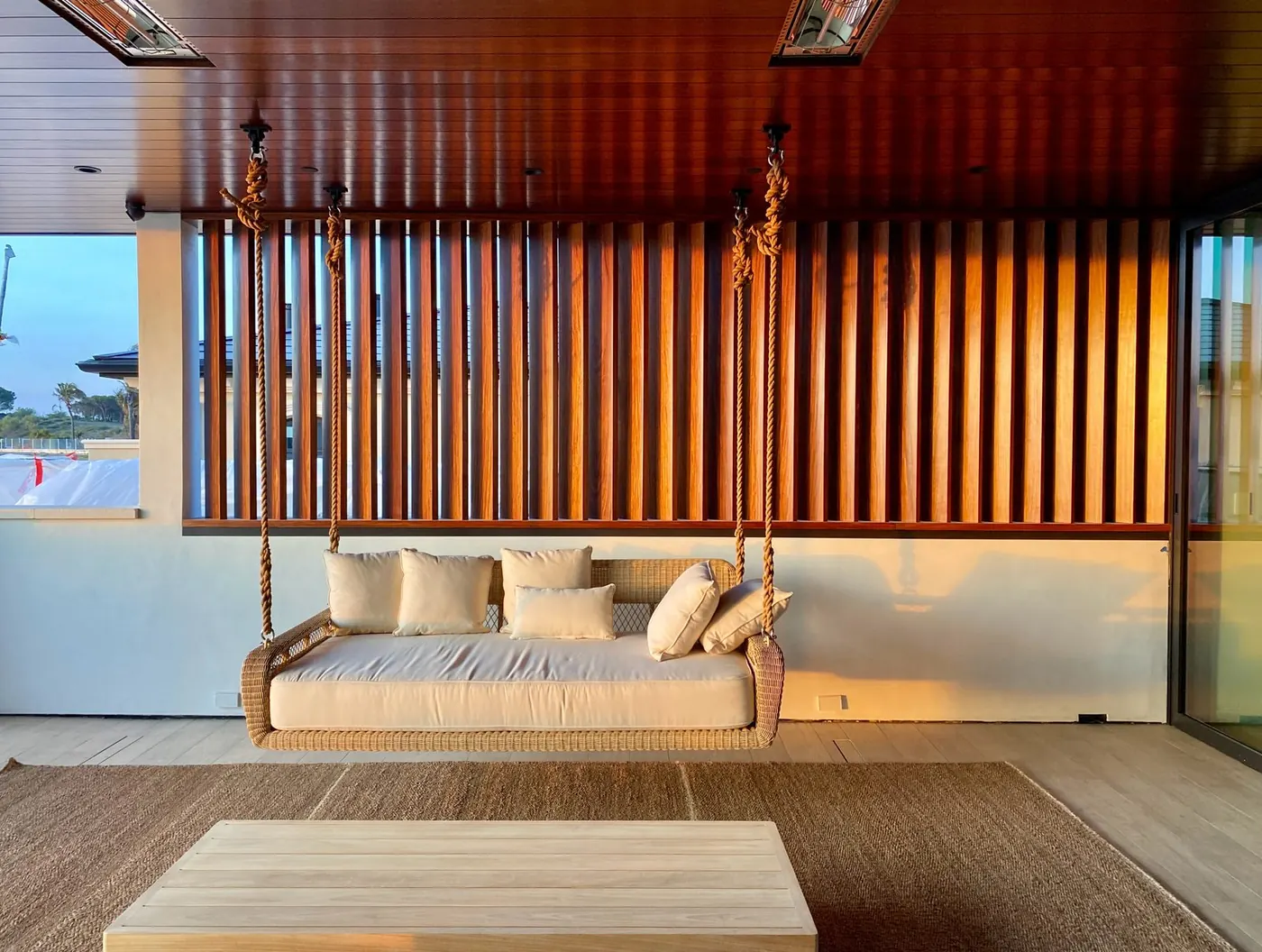 Completed Serrano Construction outdoor living space in Laguna Niguel with a hanging wicker daybed and wood-slat ceiling at sunset